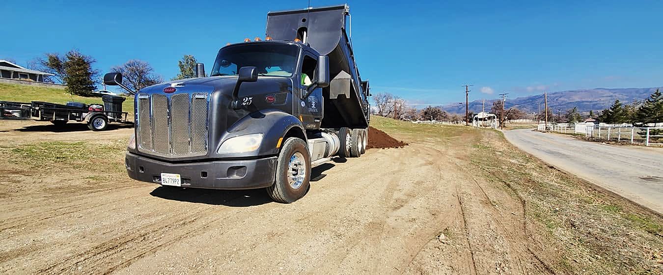 Black dump truck with its bed raised on a dirt road