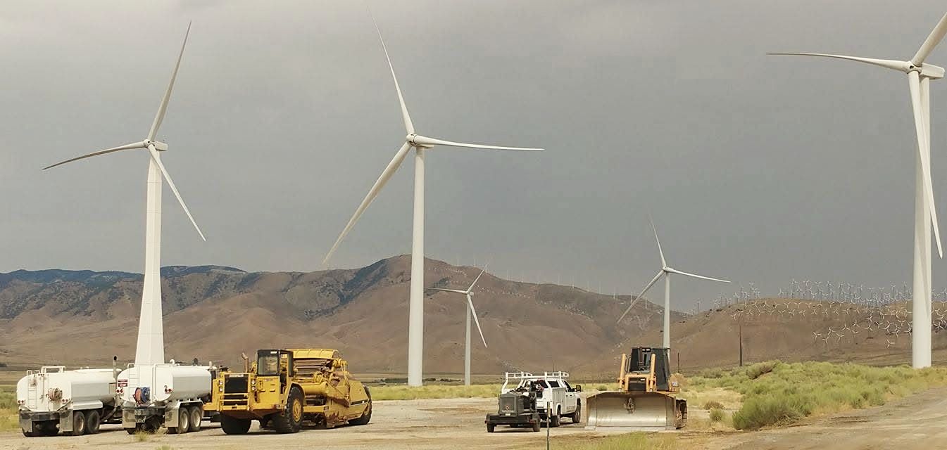 Water trucks, a scraper and a dozer parked below wind turbines